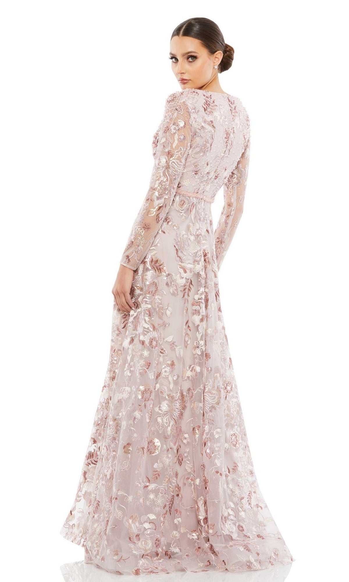 A woman in the Mac Duggal 67869 Long Sleeve Lace Formal Dress—featuring a long, pale pink floral embroidered gown with sheer sleeves—stands back-turned, looking over her shoulder; an elegant mother of the bride choice.